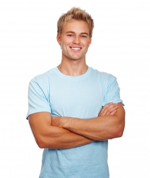 An attractive young man with blonde hair and a light blue shirt with his arms folded flashing a bright white smile because of teeth whitening in Durham, NC